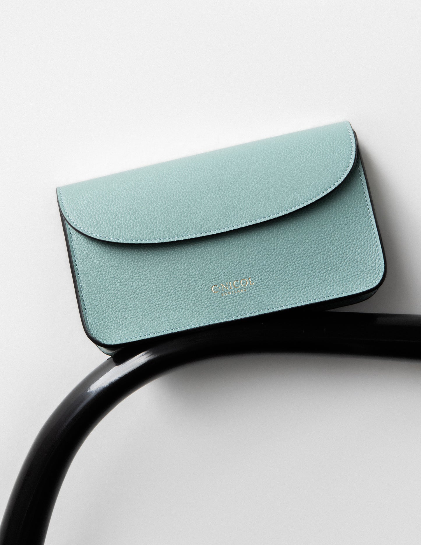 CNicol Green Leather Kate Bag sat on top of an arm of a black chair