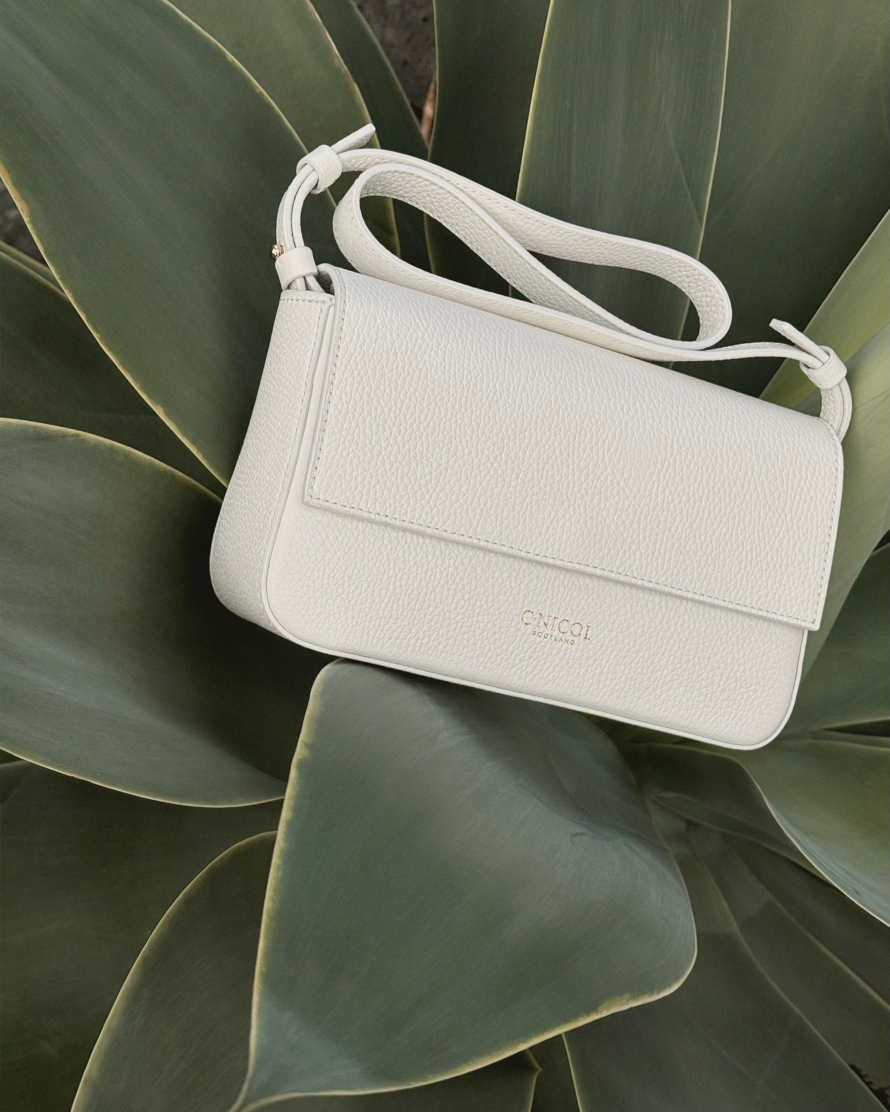 White handbag with a brand logo on a green leafy background