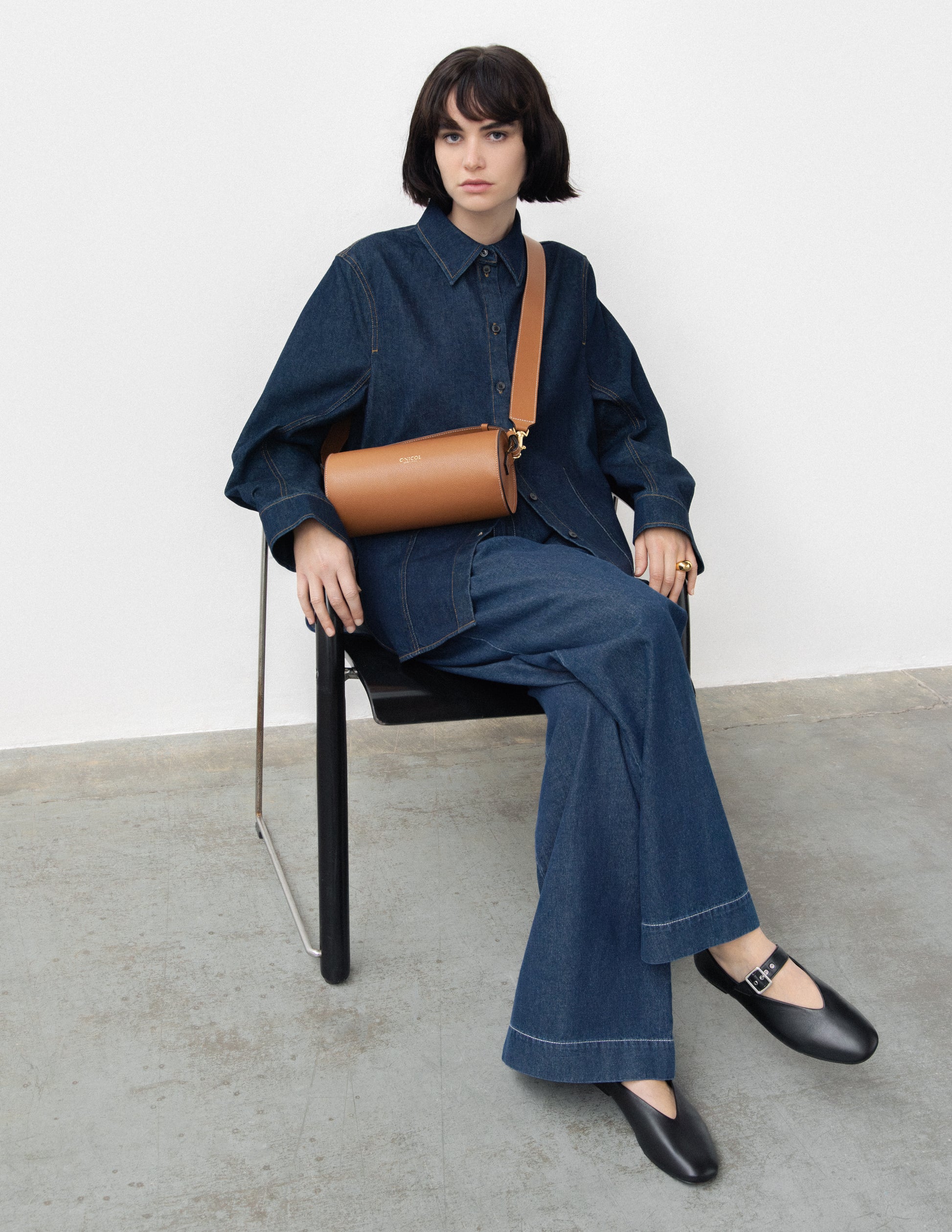 CNicol Brown Leather Bag worn by woman in denim blue shirt and trousers sat on a black and chrome chair