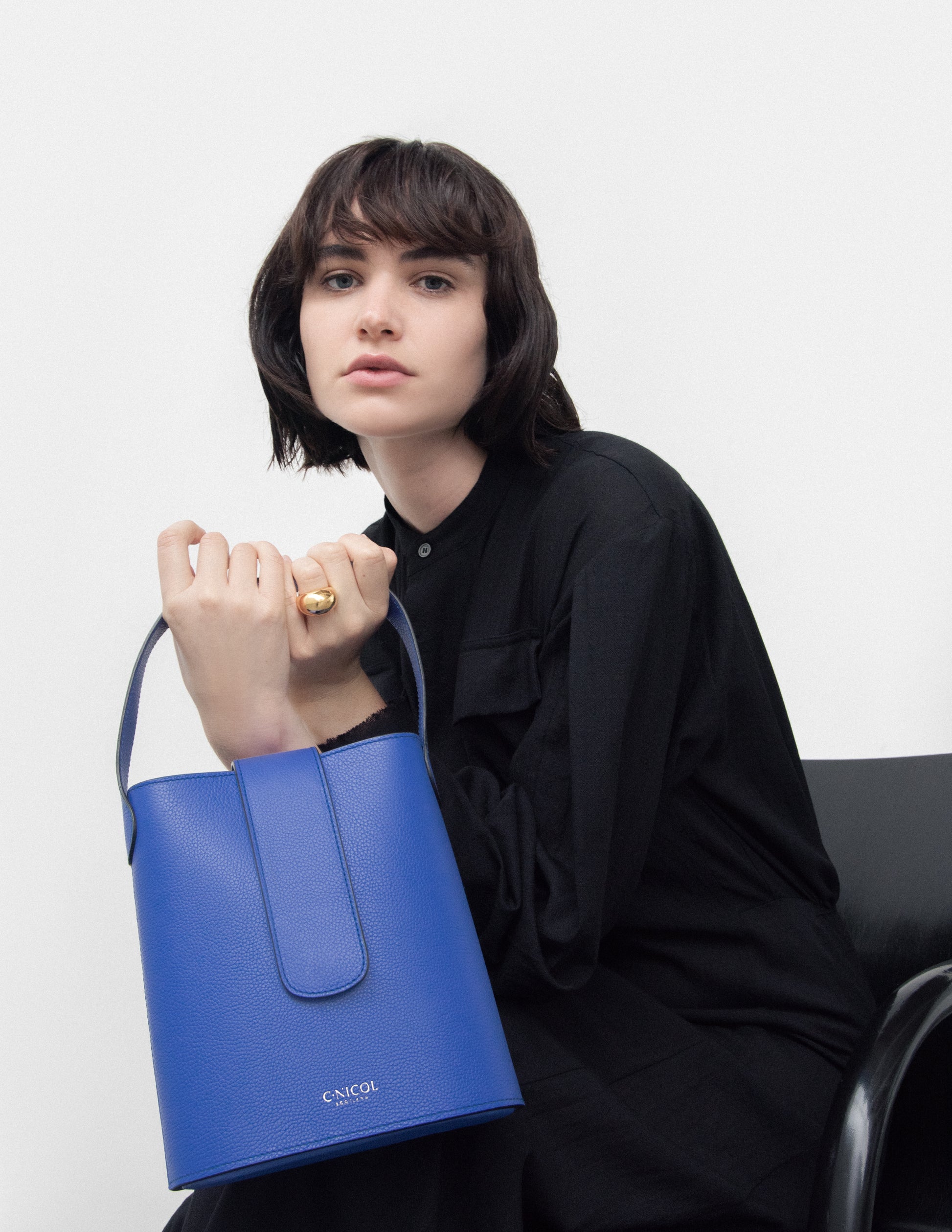 CNicol Blue Leather Holly Bag held by model dressed in all black seated on a black chair