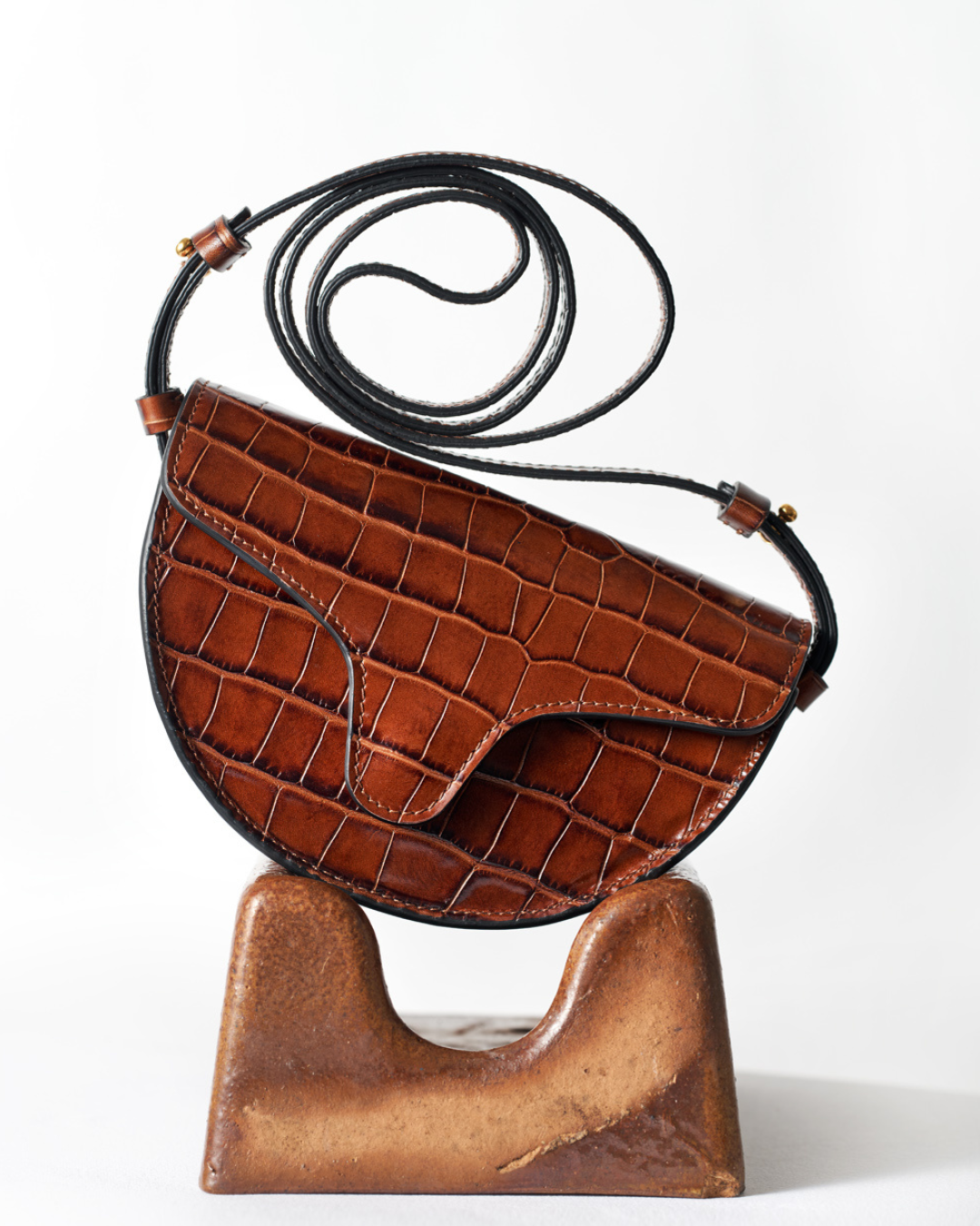 CNicol Brown Croc Leather Lily Bag on top of brown wooden holder