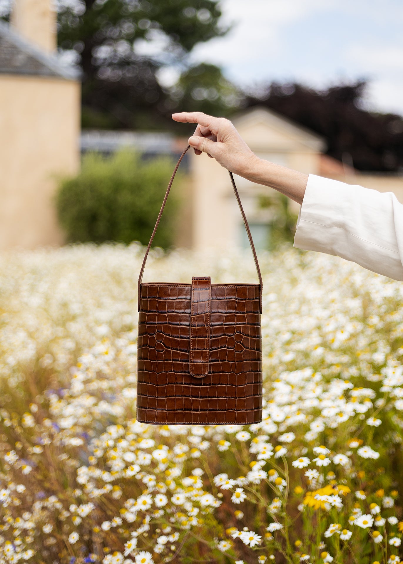C.Nicol Scotland brown croco leather bag front view, held out my a woman's arm against a backdrop of flowers