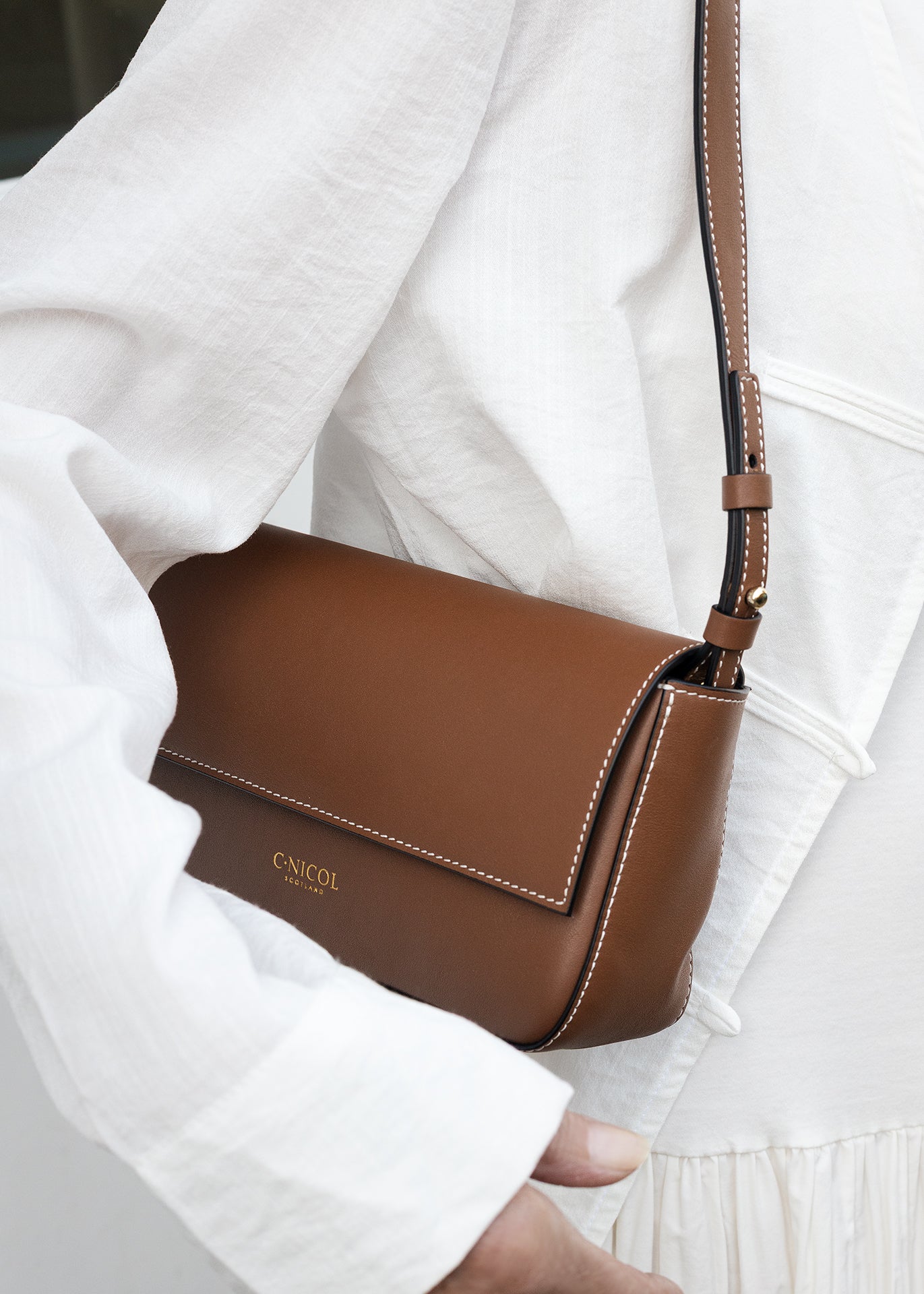 C.Nicol Scotland tan leather bag front view, on the shoulder of a woman wearing a white dress